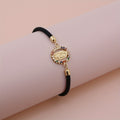 Pulsera Virgen Maria - Cordon Ajustable Banado en Oro 24K sobre superficie de madera — presentacion del producto
