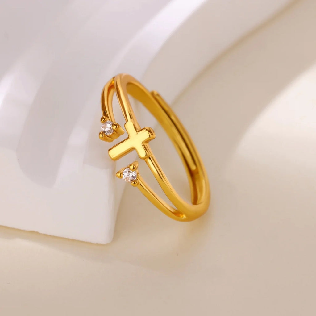 Anillo cruz con circonias dorado apoyado sobre fondo claro