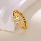 Anillo cruz con circonias dorado apoyado sobre fondo claro