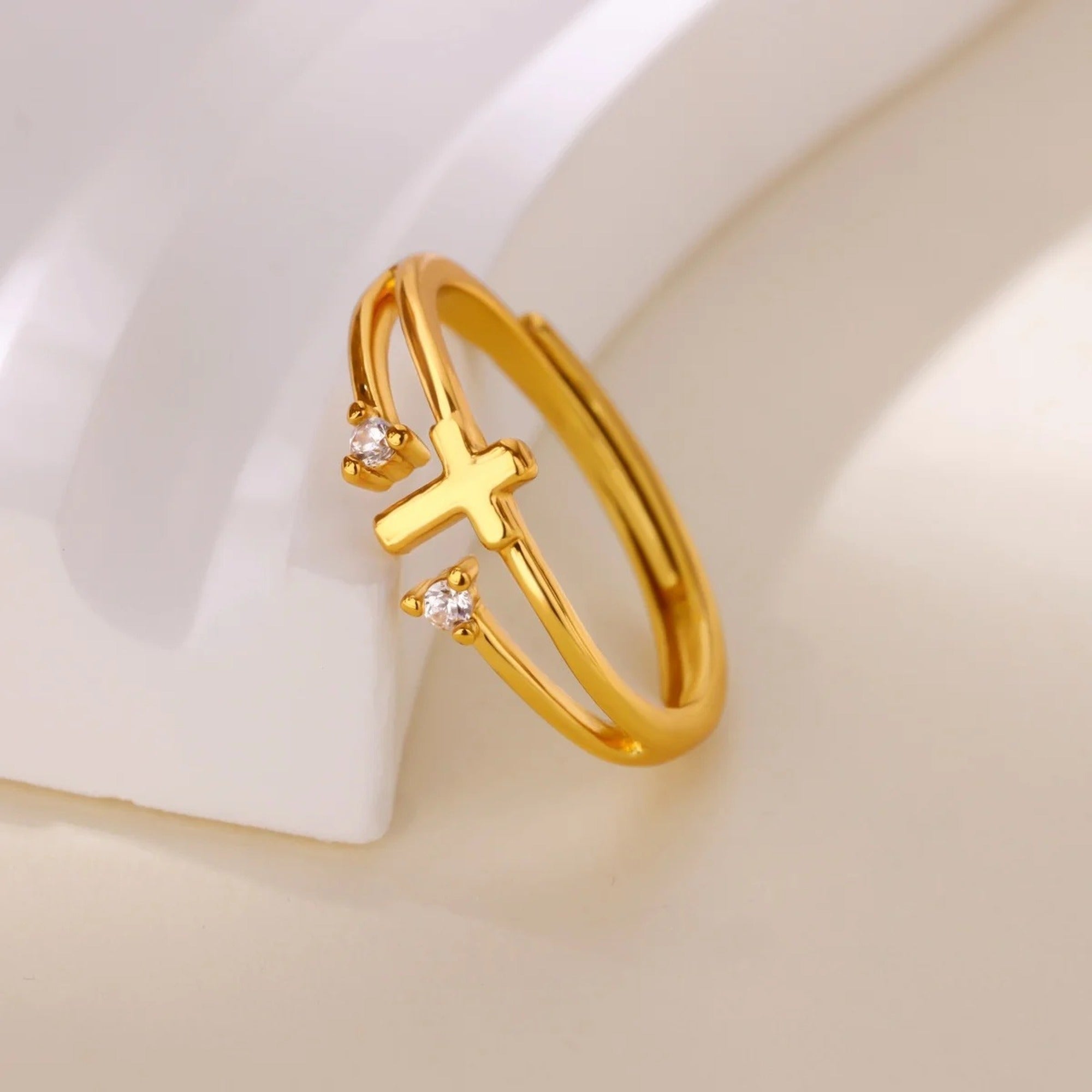 Anillo cruz con circonias dorado apoyado sobre fondo claro