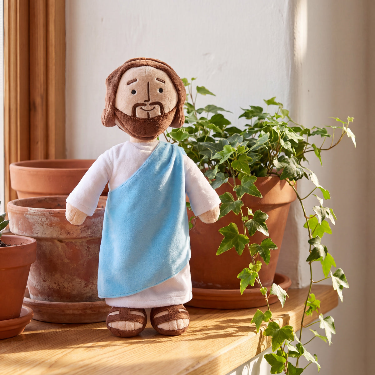 Peluche de Jesús junto a macetas de barro y hiedra en el hogar